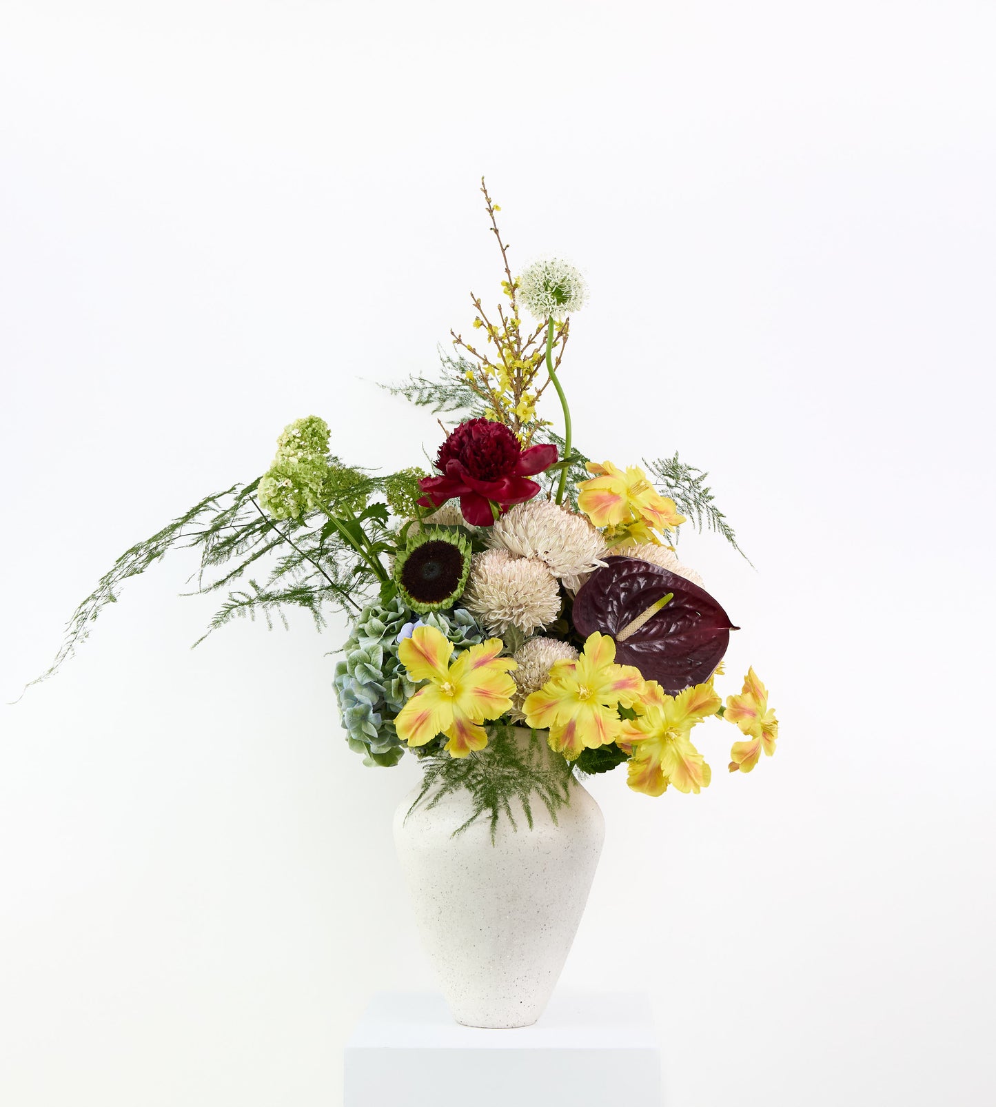 Electric Muse bouquet with yellow alstroemeria, burgundy flowers, and soft textures in a sculptural vase.