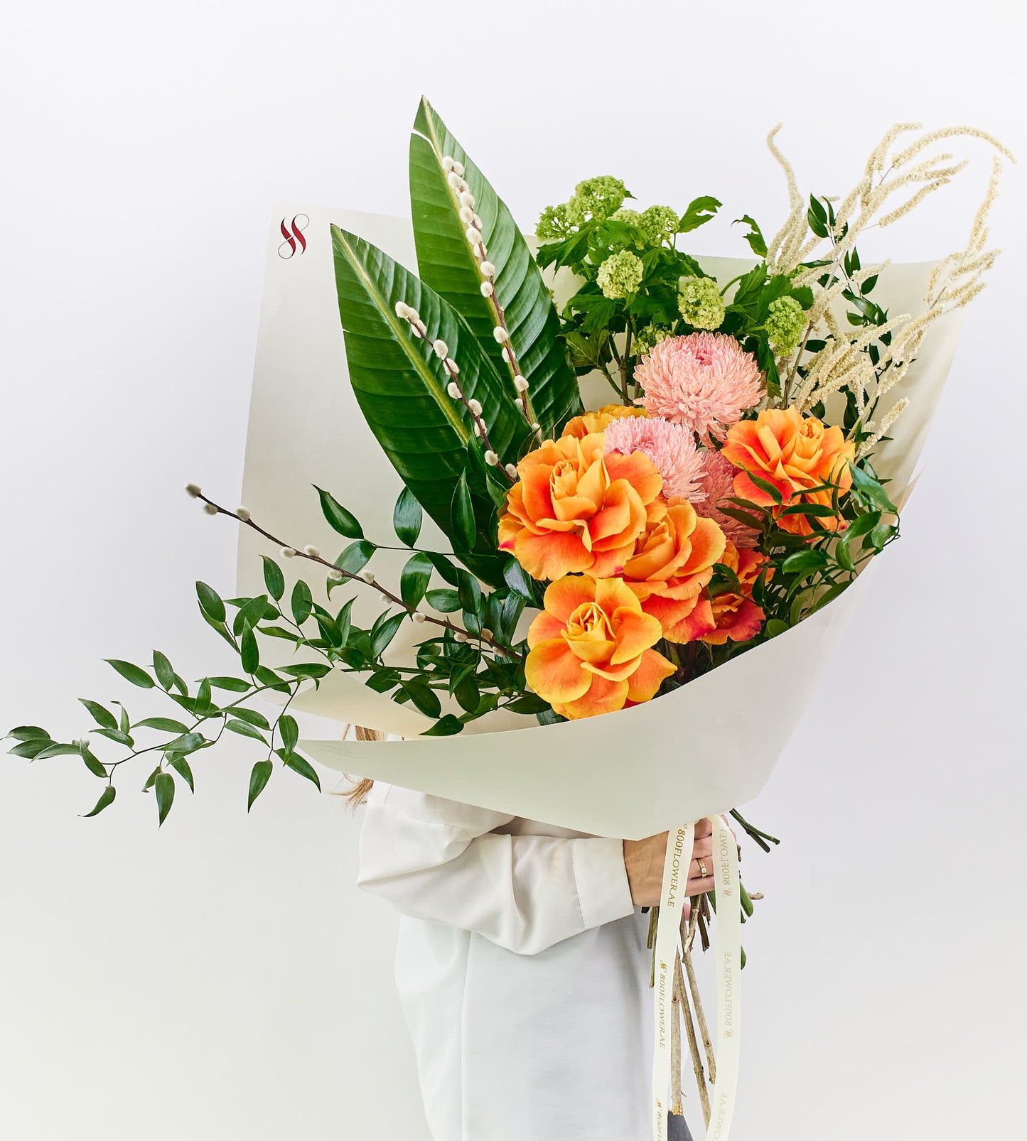 Bouquet of golden orange roses, soft pink flowers, and lush green leaves.