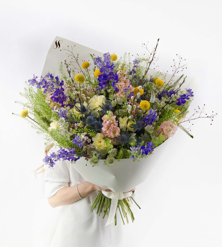 Rustic wildflower bouquet with golden craspedia, blue thistles, and pastel blooms.