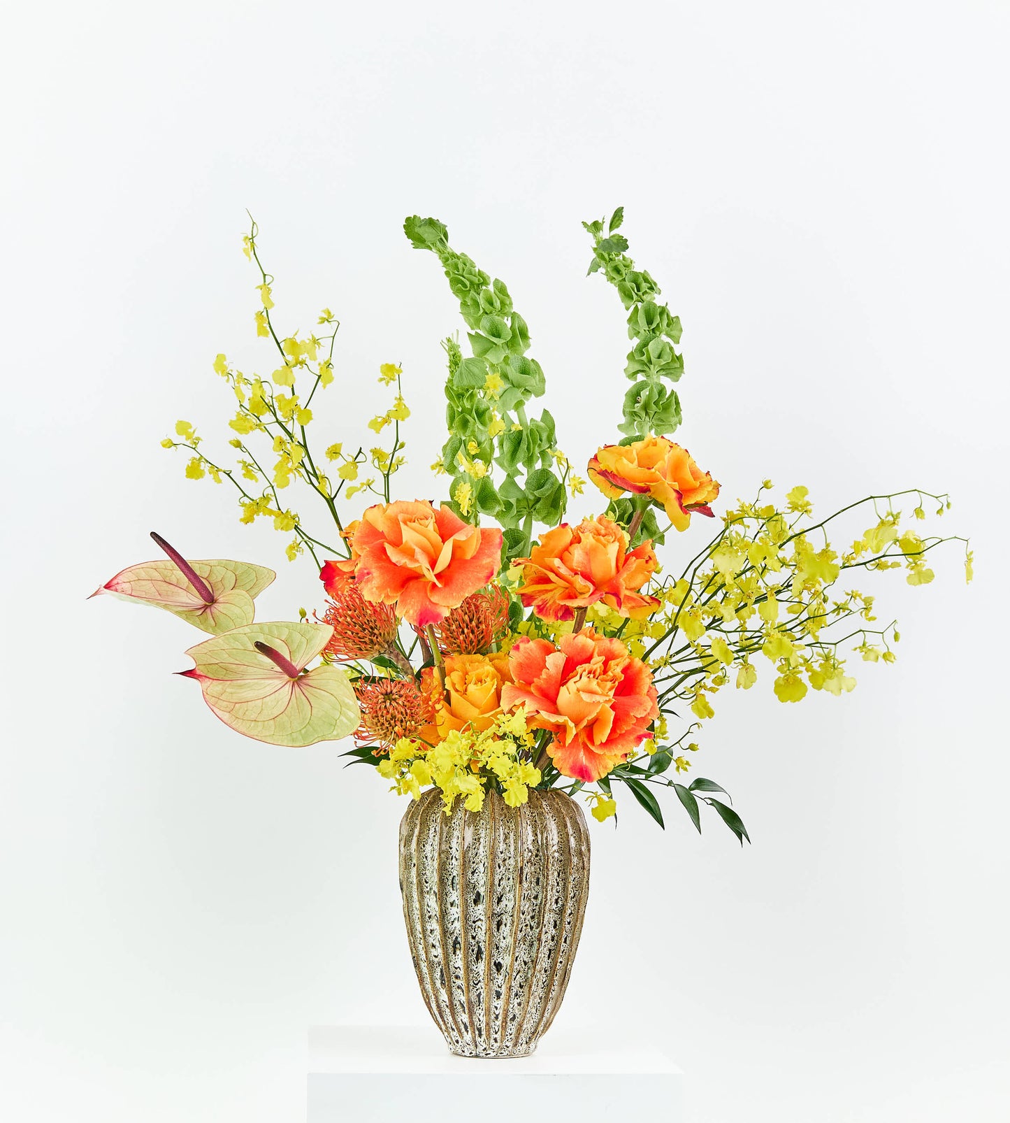 Orange roses and pincushion proteas in a textured vase.
