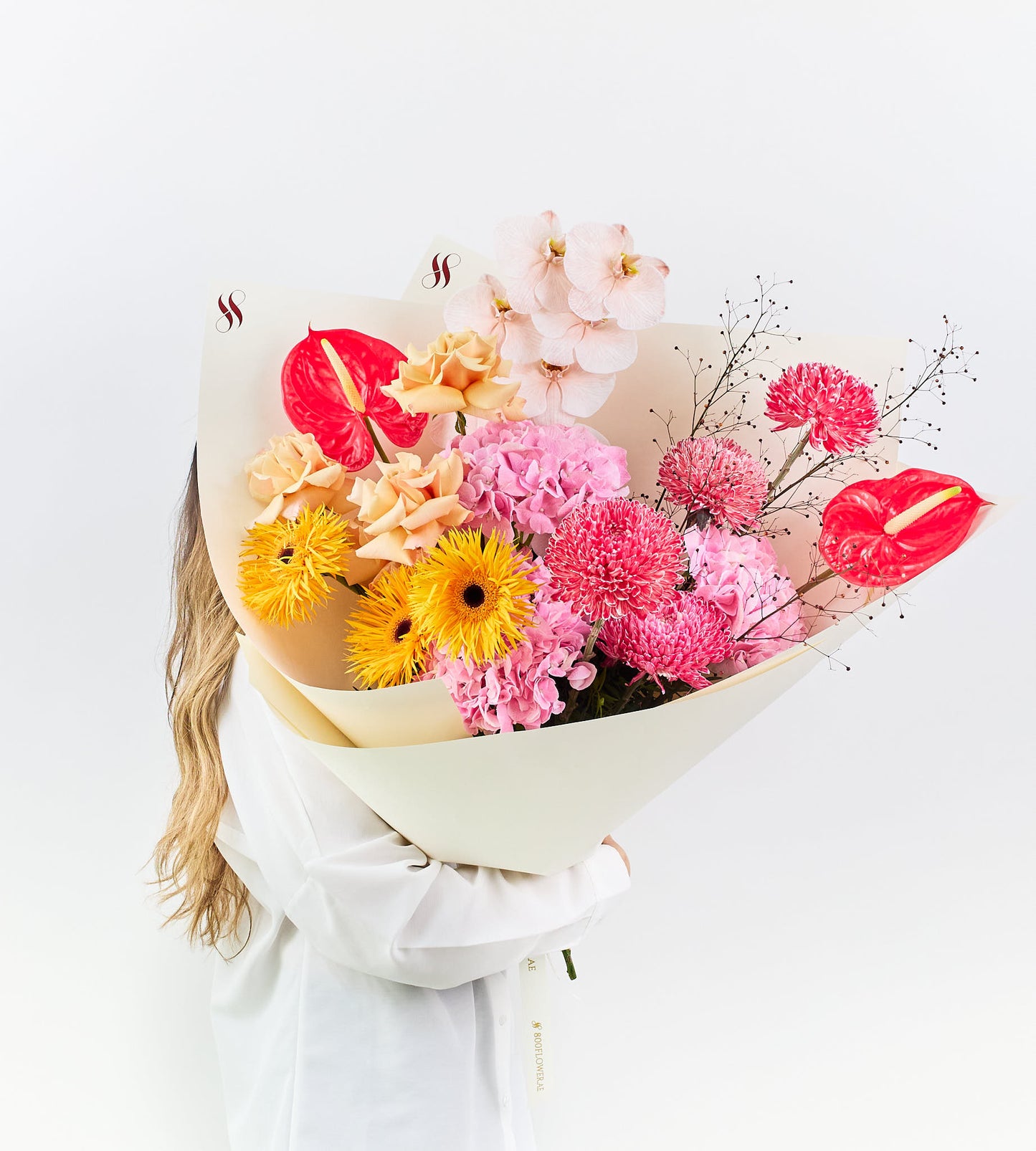 Bouquet of golden gerberas, blush orchids, and crimson anthuriums.