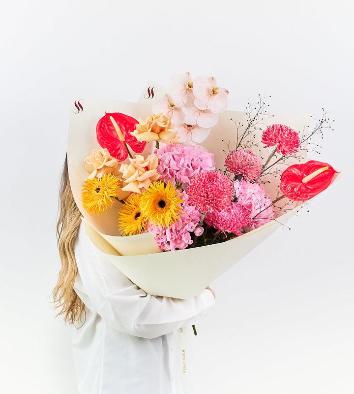 Bouquet of golden gerberas, blush orchids, and crimson anthuriums.