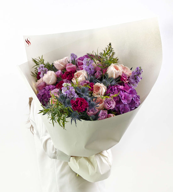 Elegant floral bouquet in blush, violet, and wine tones with soft greenery.