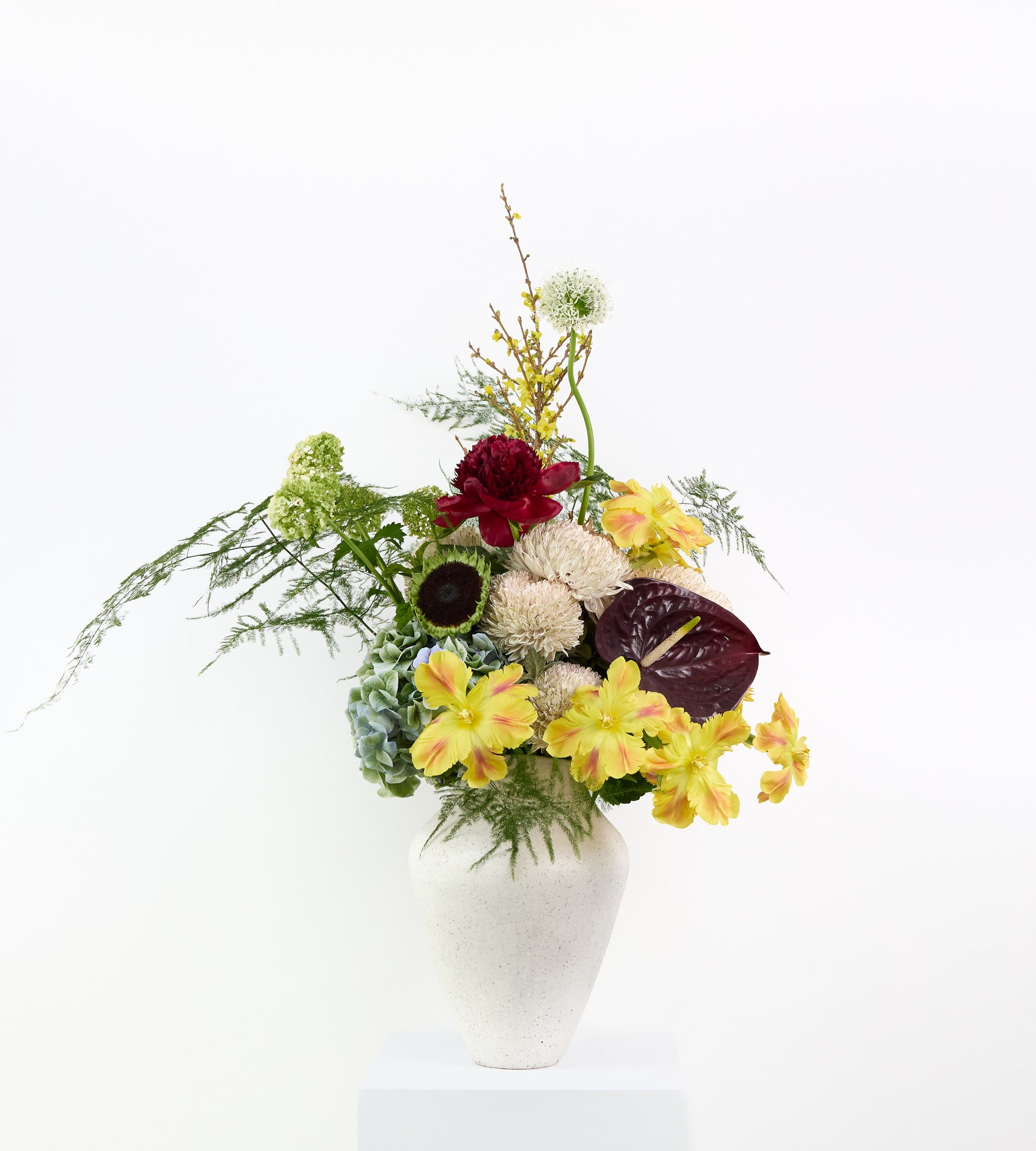 Electric Muse bouquet with yellow alstroemeria, burgundy flowers, and soft textures in a sculptural vase.