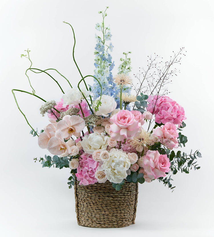Basket floral arrangement with blush flowers and soft textures, inspired by a spring garden at golden hour.