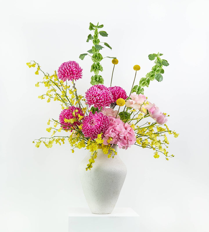 Magenta chrysanthemums, pink hydrangeas, peach roses, and yellow orchids in a speckled vase.